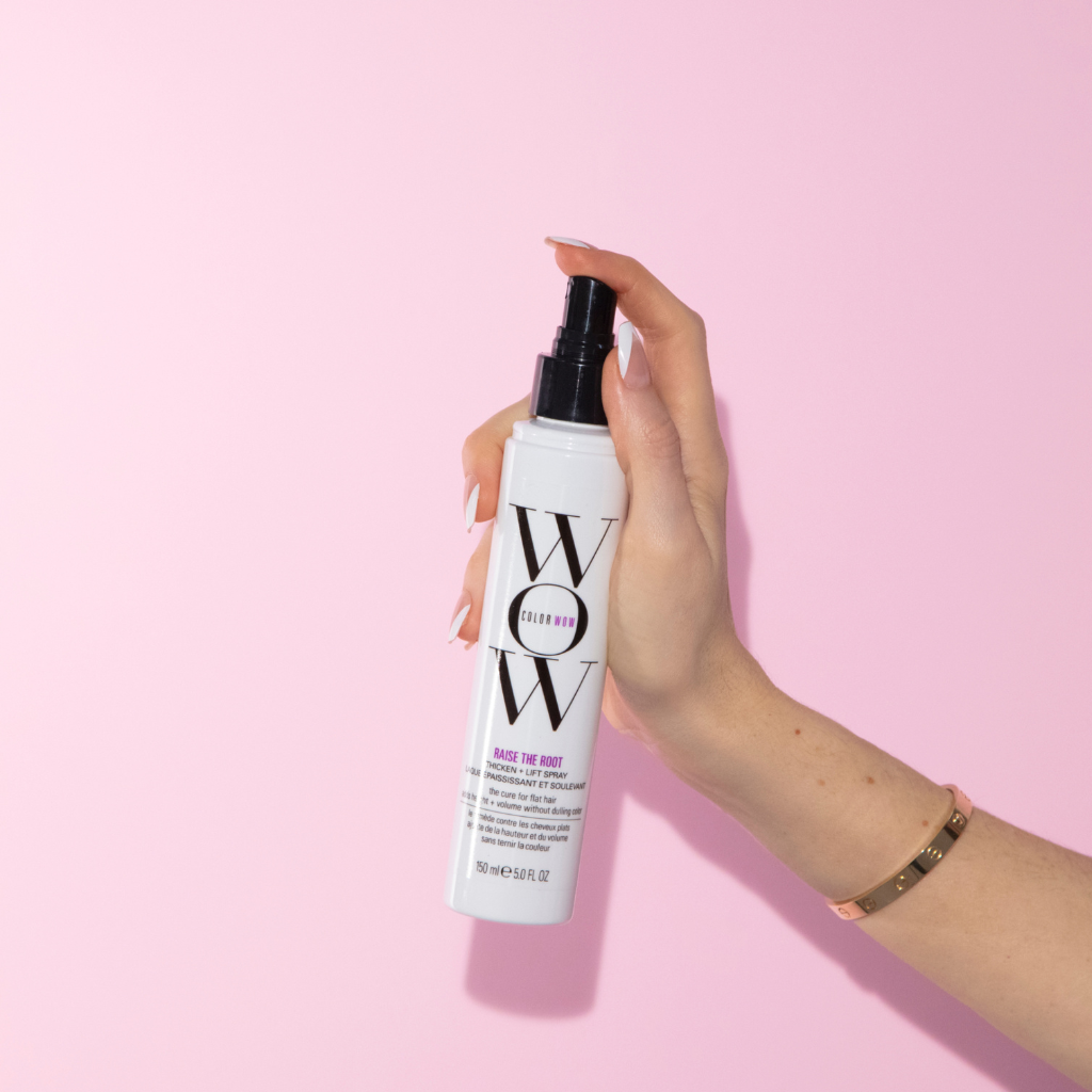 Color Wow Raise the Root Volumenspray in einer Hand vor rosafarbenem Hintergrund